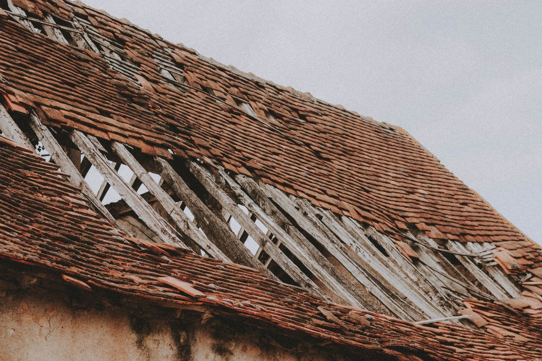 A clay-tiled barn roof with a long section of tiles torn away by wind