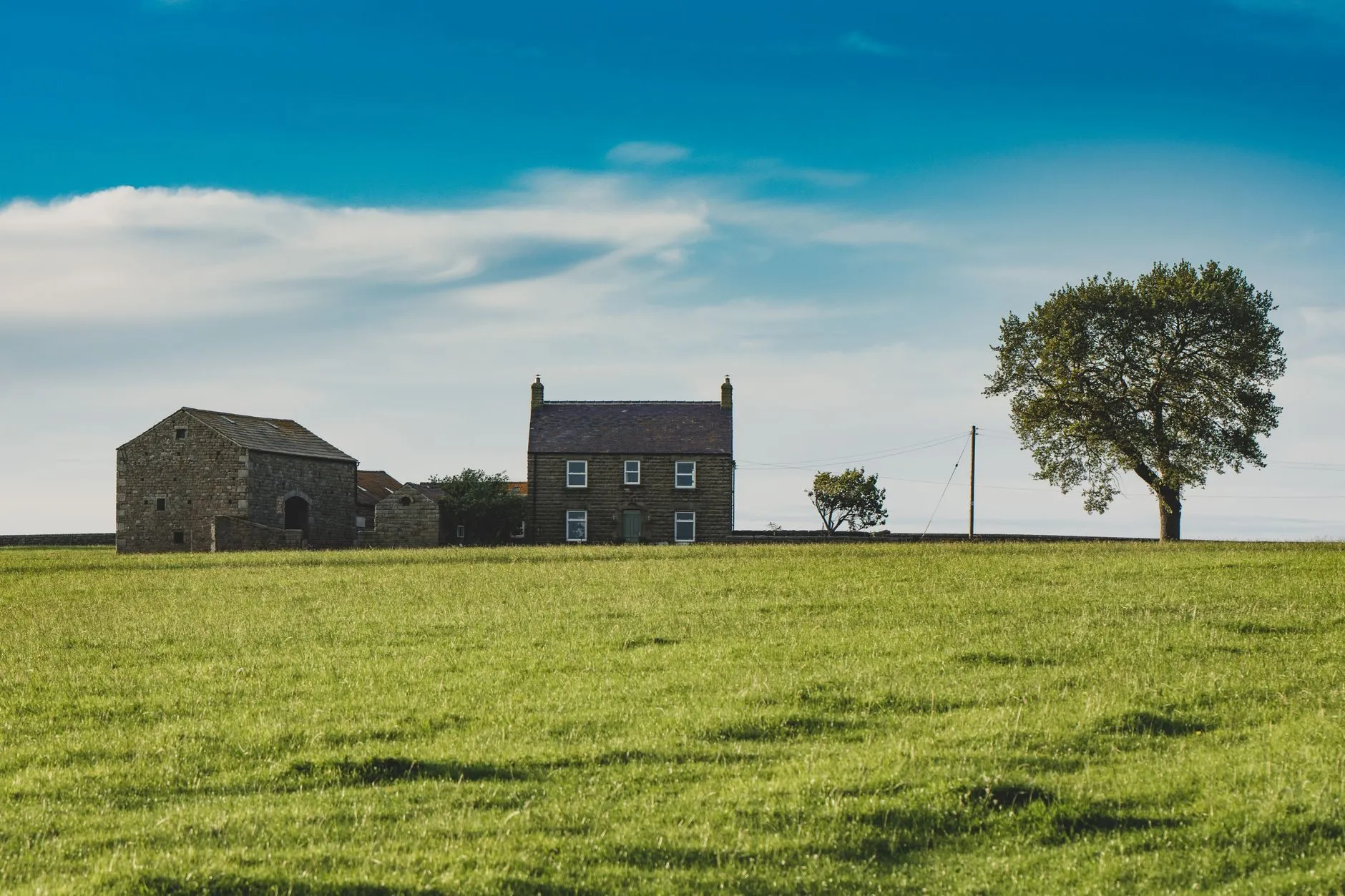 A stone farmhouse and barn on a ridge behind a wide green field