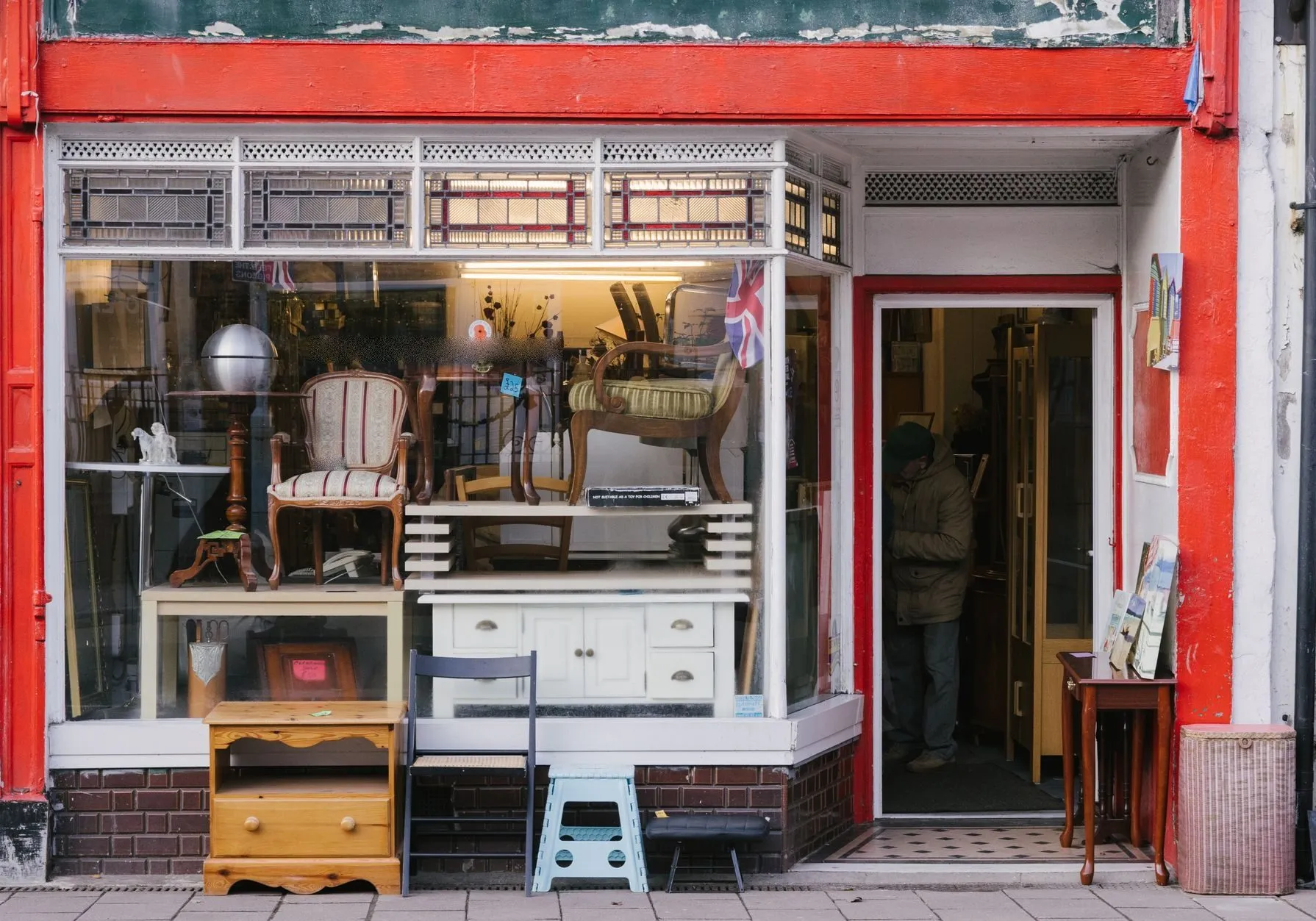 A red-painted shopfront with chairs and cabinets displayed in the window