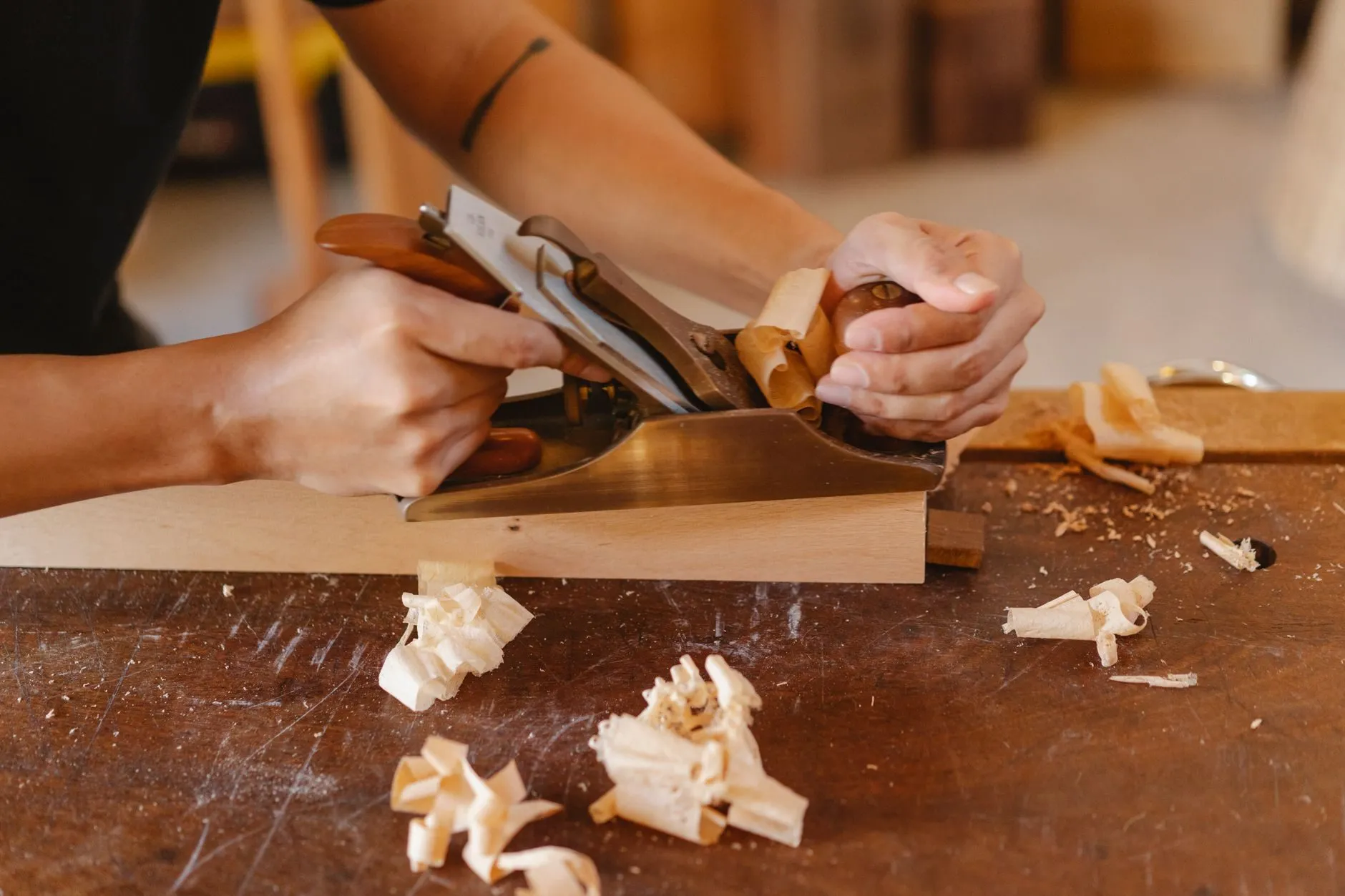 Hands pushing a brass hand plane along a length of beech, shavings on the bench