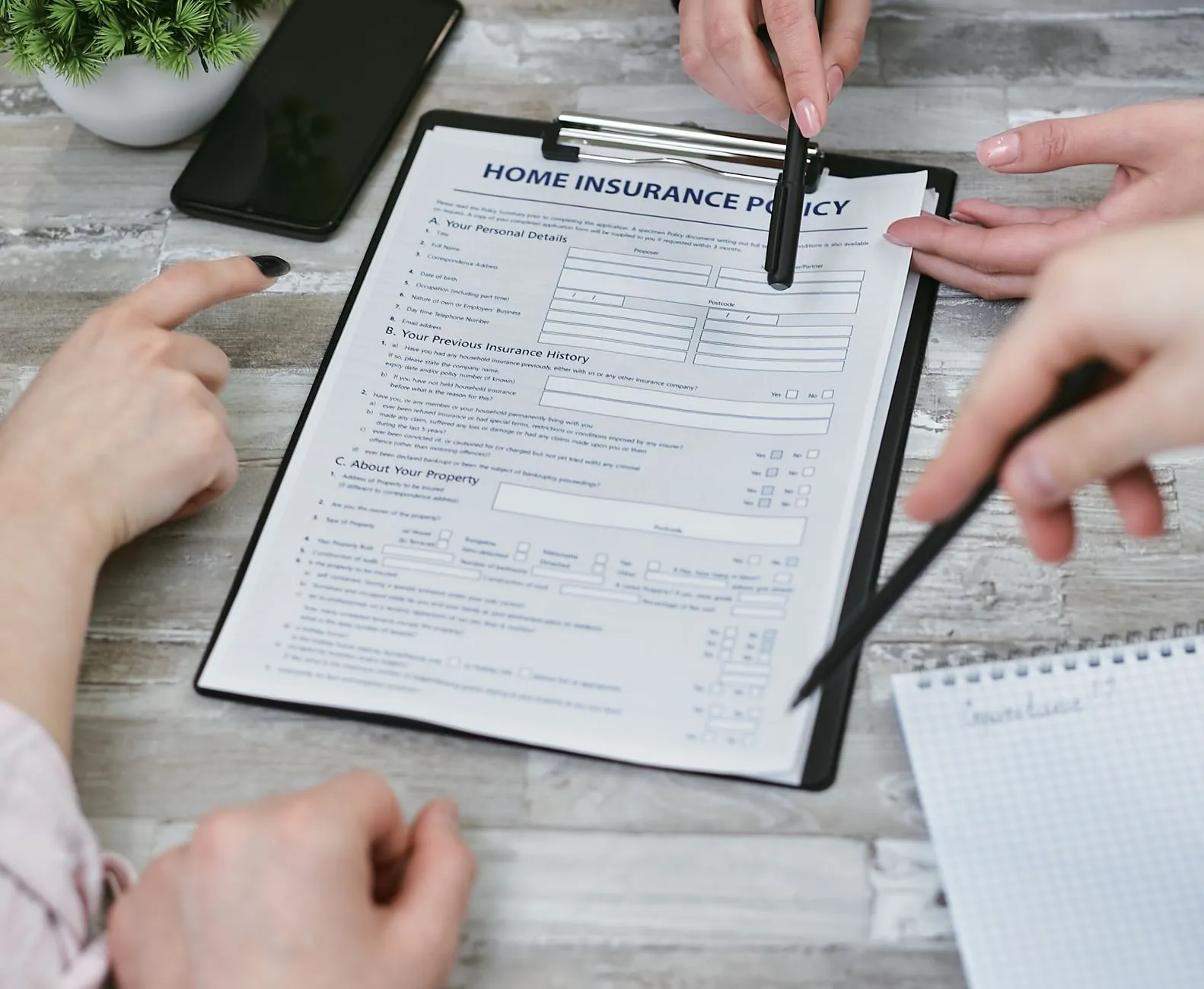 Two people's hands going through a home insurance form on a clipboard