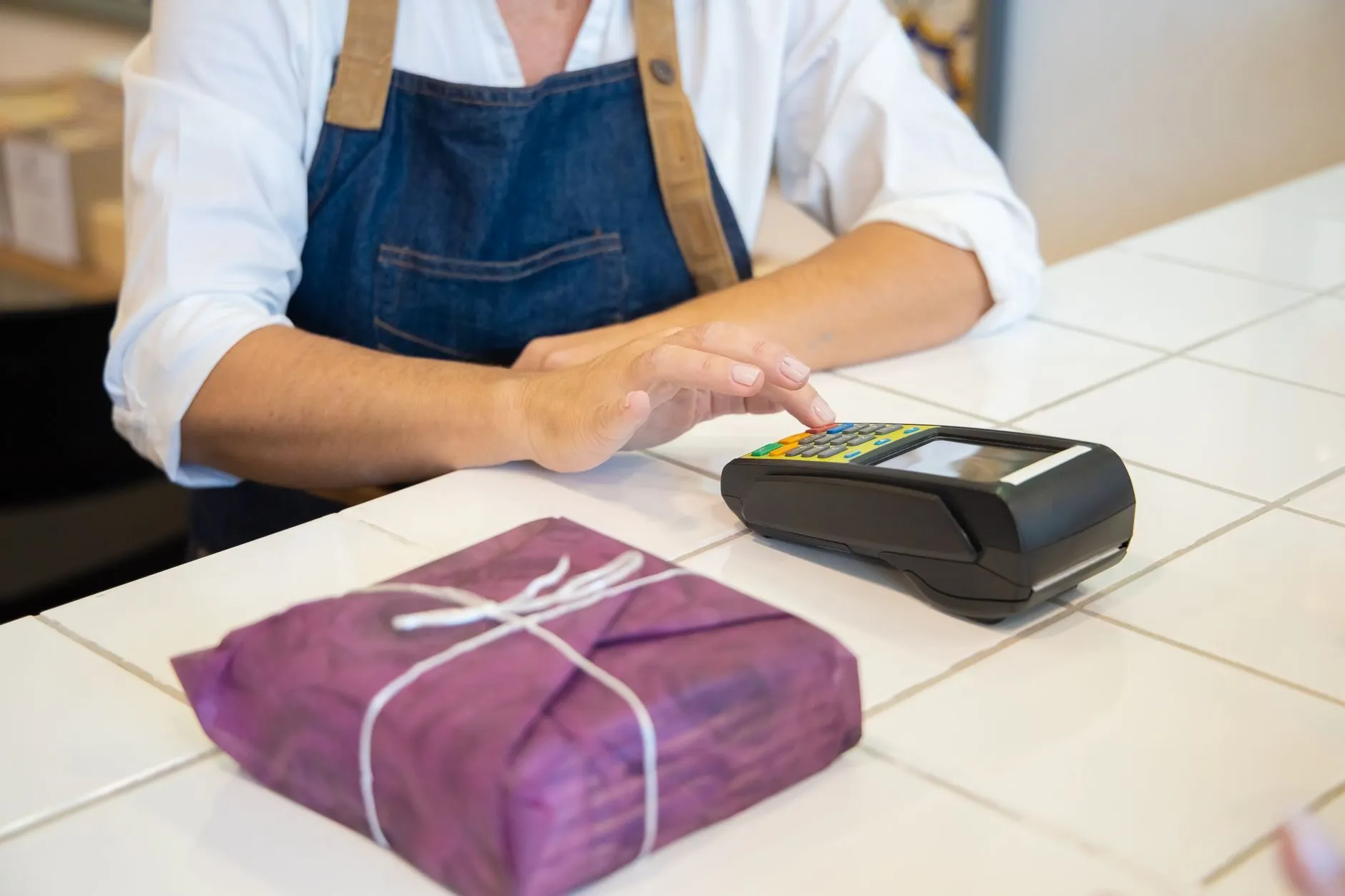 A shopkeeper's hands at a card reader beside a wrapped parcel on the counter