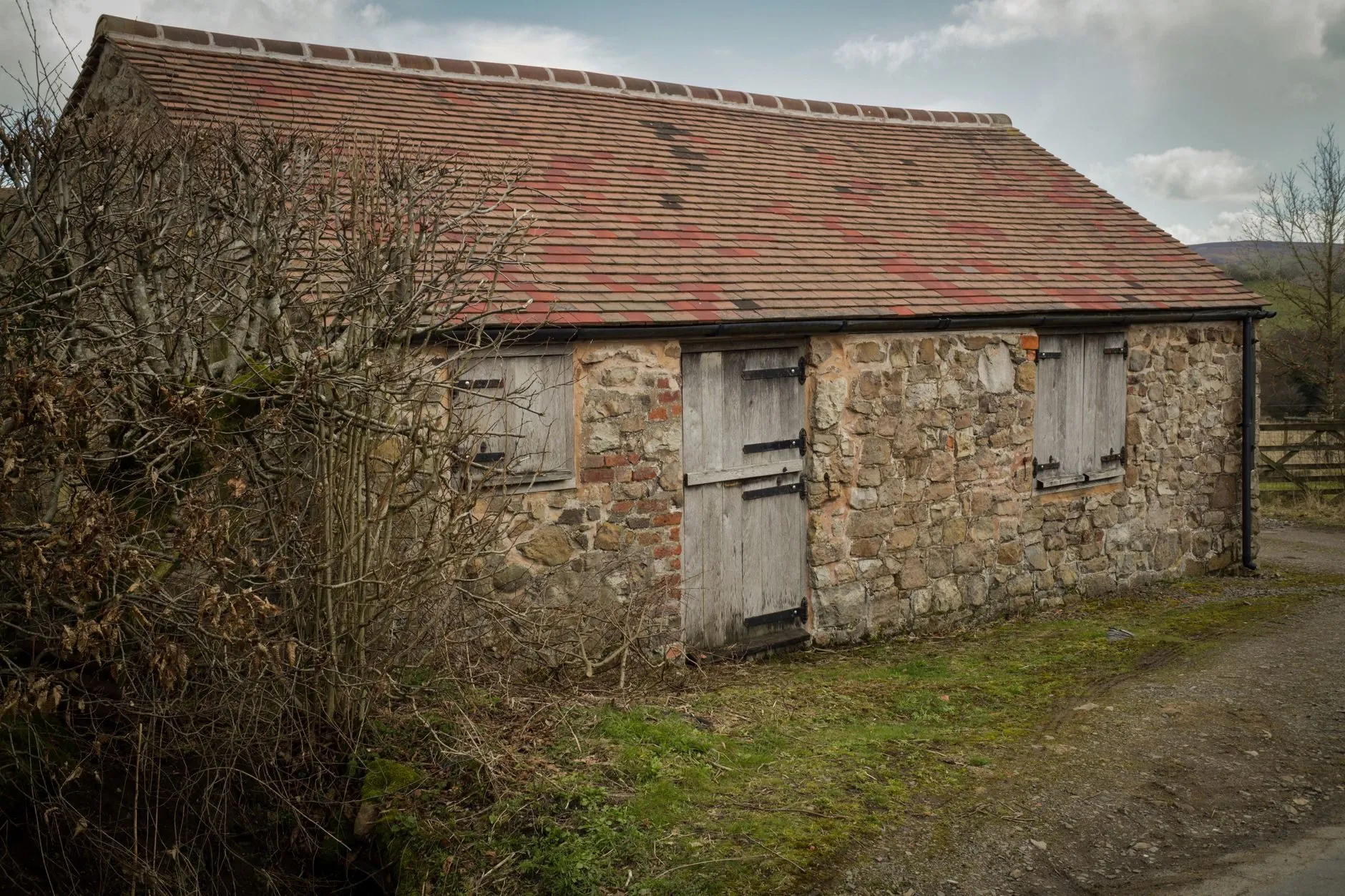A stone barn with weathered wooden doors beside a farm track