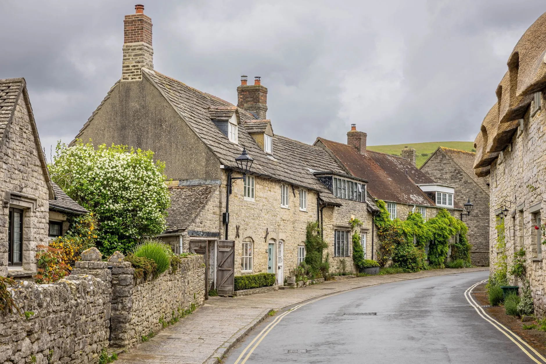 A curving village street of stone cottages with tiled roofs under a grey sky