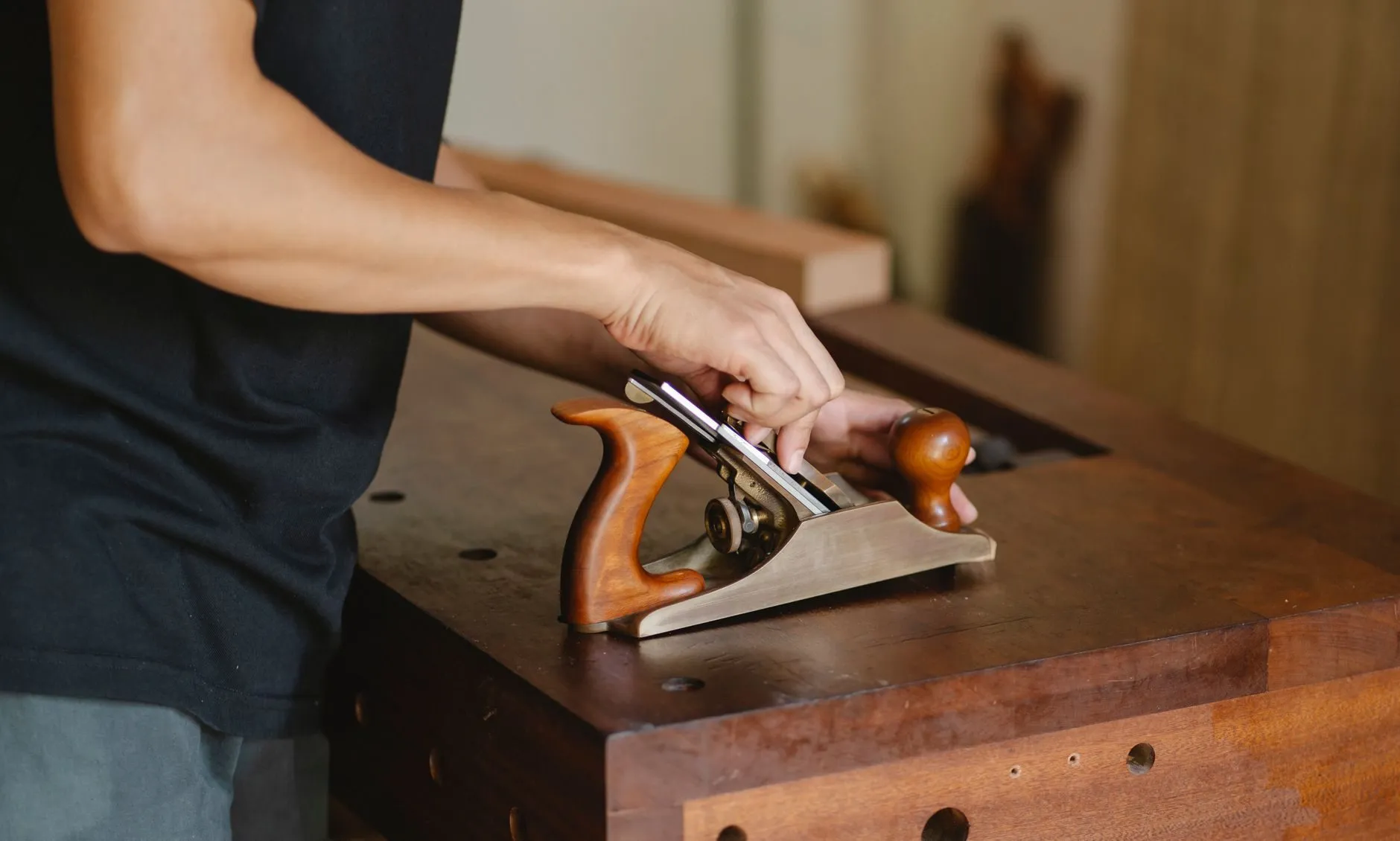 Hands on a wooden-handled plane at a workbench
